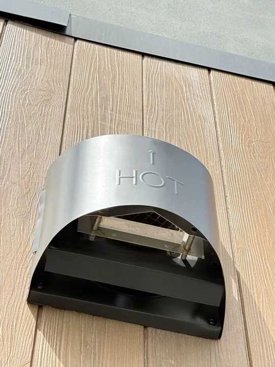 After: stained and marked stainless steel cowl on an external timber-look wall