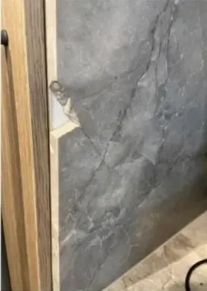 Before: chip on the edge of a dark grey stone wall panel beside timber joinery