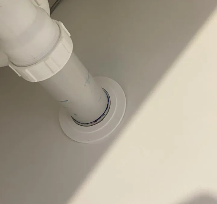 After: oversized hole cut around a white waste pipe in a cabinet panel