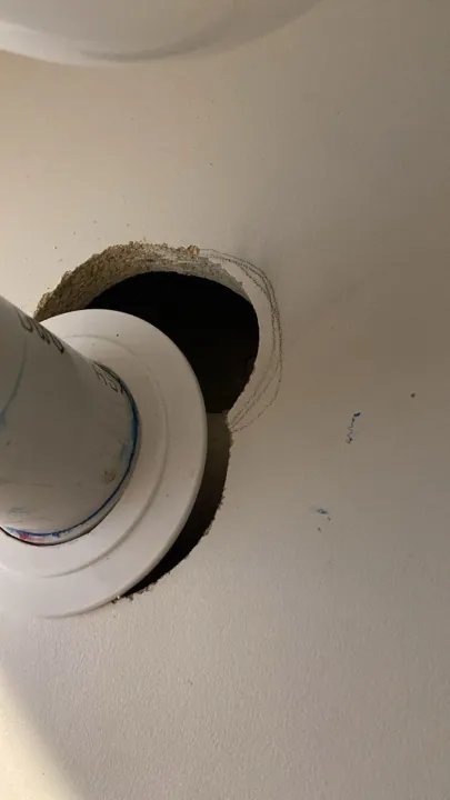 Before: oversized hole cut around a white waste pipe in a cabinet panel