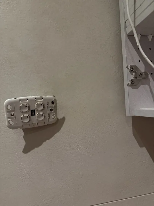 After: rough cut-out in a plaster wall with cabling exposed beside a switch plate