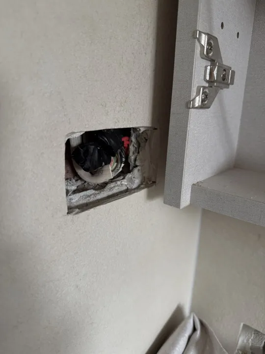 Before: rough cut-out in a plaster wall with cabling exposed beside a switch plate