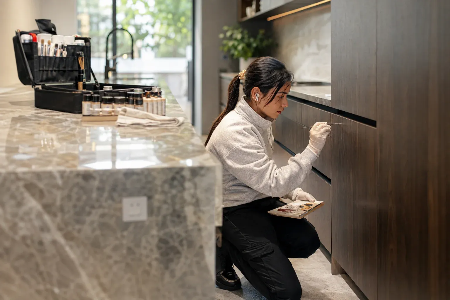 Our technician touching up a dark timber kitchen drawer front beside a marble benchtop in a Sydney home